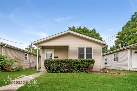 a small tan house with a yard and a green lawn